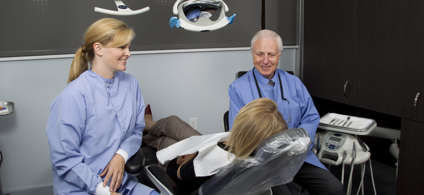 Dr. Gordon J. Christensen (right) and his assistant (left) sit chairside, consulting a dental patient (seated, center).